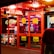 A brightly lit entrance to a casino with neon signs, including one advertising a £500 jackpot. The doors have clear signage indicating entry is restricted to those over 18. A person in a red jacket stands to the right, possibly interacting with a machine or display.